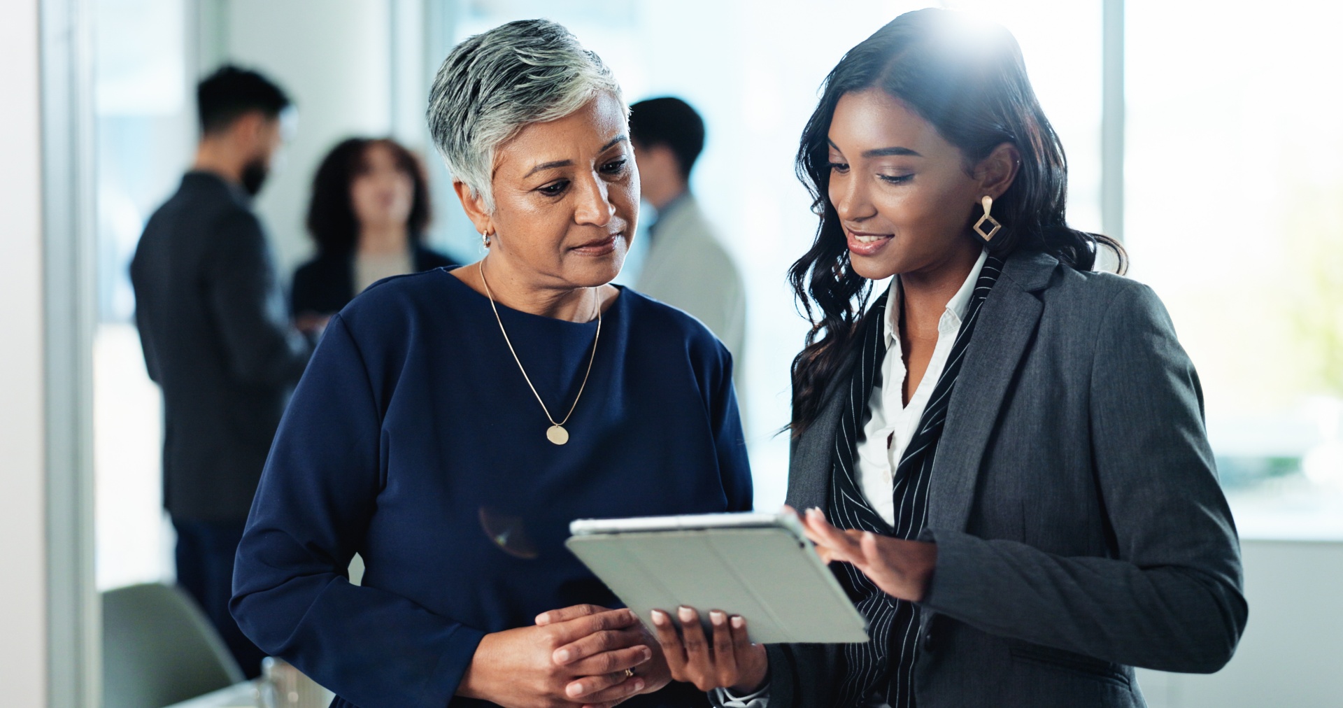 Two businesswomen discussing work while reviewing information on a tablet